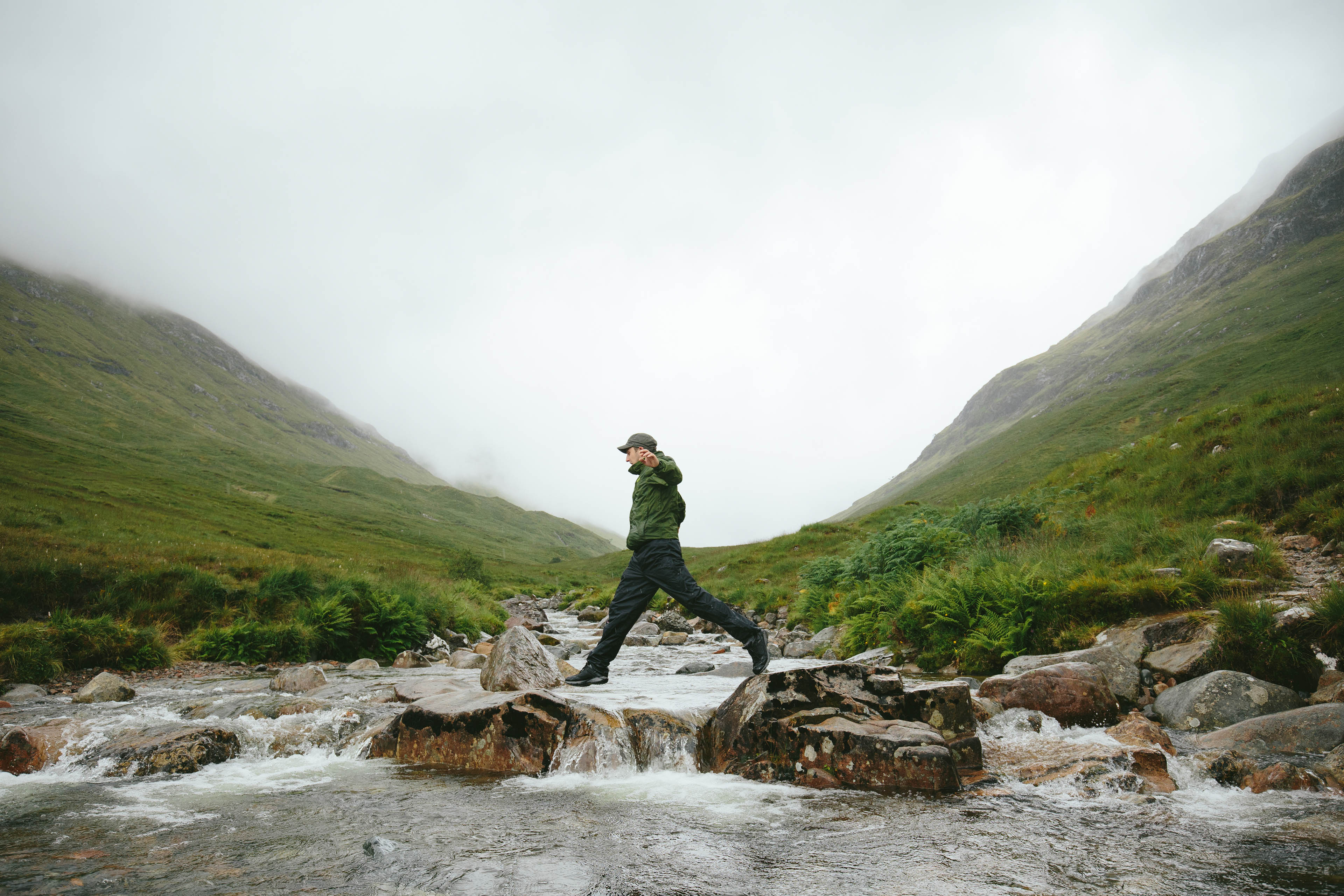 Hiker crossing river in mountain valley Glencoe Scotland